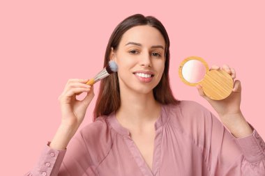 Beautiful young woman holding brush and highlighter on pink background