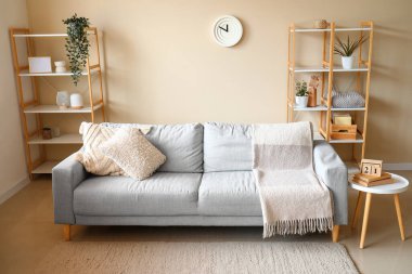 Interior of modern living room with grey sofa, table and wooden racks near white wall