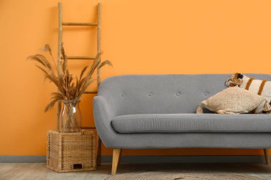 Yastıklı gri kanepe ve şeftali duvarının yanında tahta merdiven.