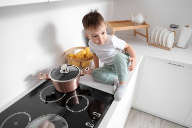 Küçük çocuk mutfakta elektrikli ocağın yanında. Tehlikedeki çocuk