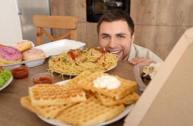 Mutfakta sağlıksız yemekleri olan genç bir adam. Aşırı yeme kavramı