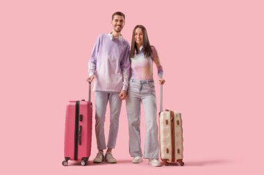 Beautiful young happy couple of tourists with suitcases and headphones on pink background