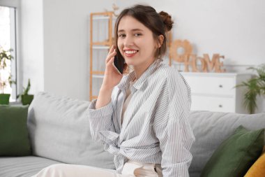 Beautiful young woman talking on phone in living room