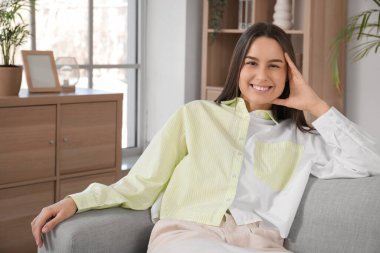 Oturma odasındaki gri kanepede oturan güzel genç bayan.