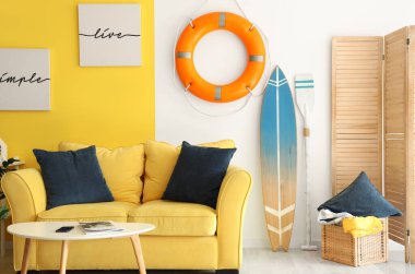 Lifebuoy, surfboard and paddle in interior of living room. Summer composition