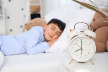 Cute little boy with alarm clock and toys sleeping in bedroom