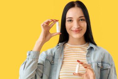 Young woman with eye drops on yellow background, closeup