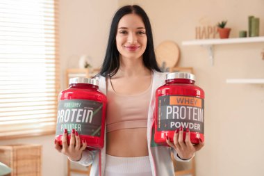 Sporty young woman with jars of protein powder at home