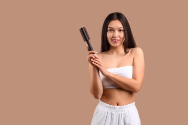 Beautiful young happy Asian woman with brush on brown background