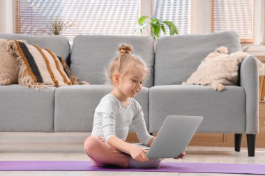 Cute little girl watching online gymnastics tutorial video on laptop at home