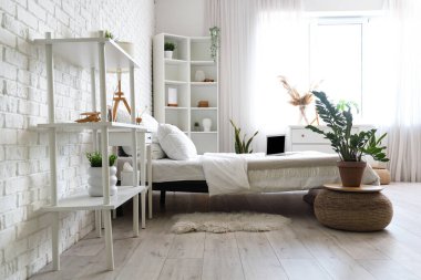 Interior of light bedroom with houseplant and laptop on white bed