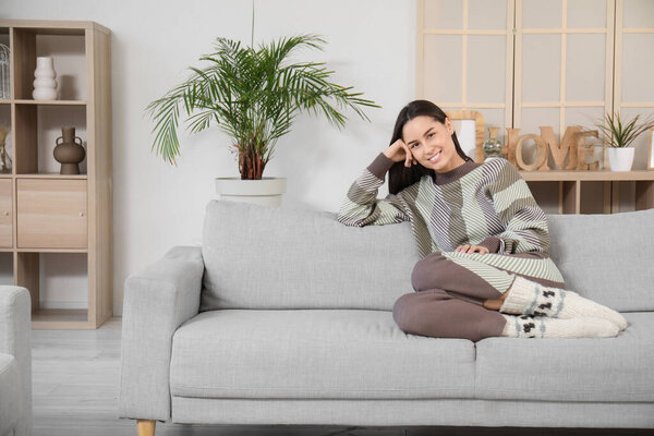 Красивая молодая женщина сидит на сером диване в гостиной