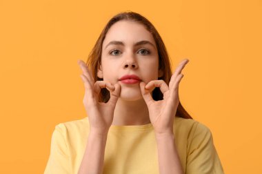 Young deaf mute woman using sign language on orange background
