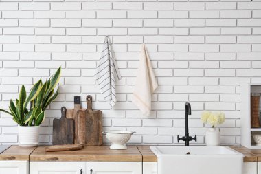 Ahşap mutfak tezgahları lavabo, çatal bıçak ve beyaz tuğla duvarın yanındaki bitki örtüsü.