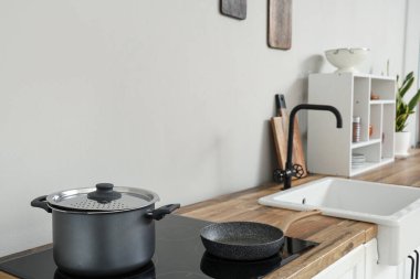 Electric stove with cooking pot and frying pan on wooden kitchen counter