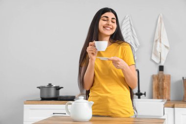 Pretty young woman with cup of tea in light kitchen