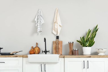 White kitchen counters with sink, utensils and houseplant near white brick wall
