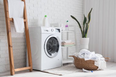 Çamaşır makinesi, hasır sepeti ve merdiveni olan çamaşır odasının içi.