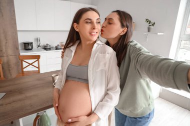 Genç hamile lezbiyen çift mutfakta selfie çekiyor.