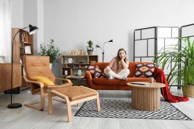 Evdeki kırmızı kanepede oturan genç kadın.