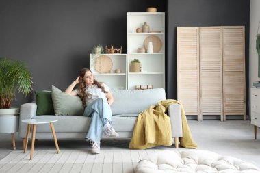 Oturma odasındaki gri kanepede oturan genç kadın.