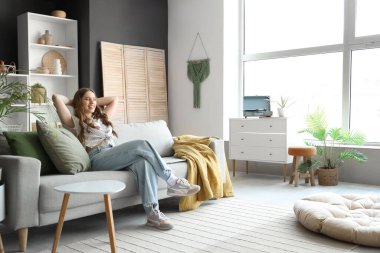 Oturma odasındaki gri kanepede dinlenen genç kadın.