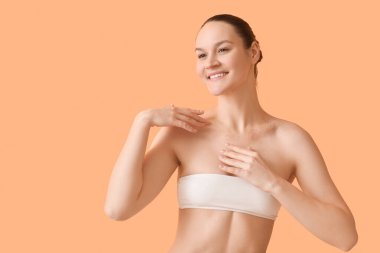 Happy young woman applying scrub on body against orange background