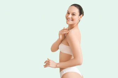 Young woman applying body scrub on shoulders against light background