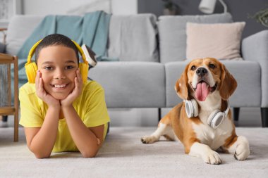 Little African-American boy and cute beagle dog with headphones lying on carpet at home