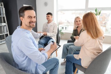 Male psychologist writing in clipboard at group therapy session