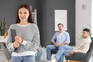 Female Asian psychologist with clipboard at group therapy session