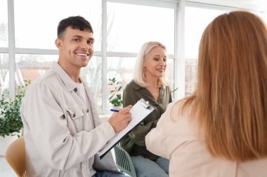 Male psychologist writing in clipboard at group therapy session
