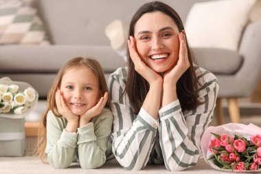 Mutlu bir anne, tatlı küçük kızı ve evde yerde yatan laleleri.