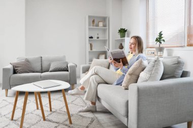 Oturma odasındaki kanepede dergi okuyan genç bir kadın.