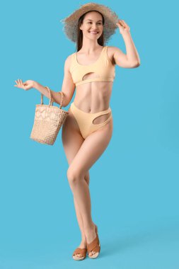 Mavi arka planda şapkası ve çantası olan bikinili kadın.