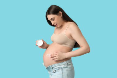 Pregnant woman applying body cream on her belly against color background