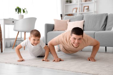 Young man and his little son doing push-ups in living room