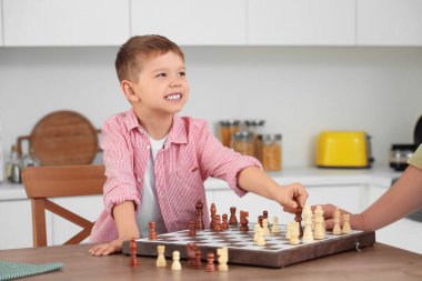 Young man and his little son playing chess in kitchen