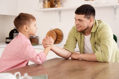 Young man with his little son having arm wrestling in kitchen