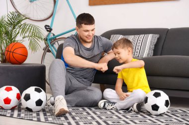Young man with his little son with football balls bumping fists at home