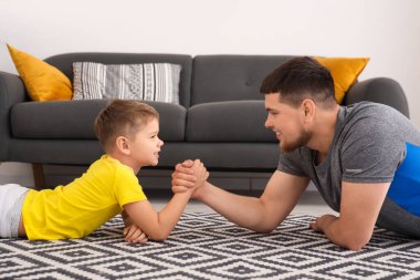 Young man with his little son having arm wrestling on floor at home