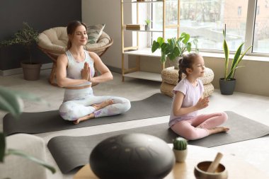 Küçük kızıyla birlikte evde yoga minderleri üzerinde meditasyon yapan genç bir kadın.