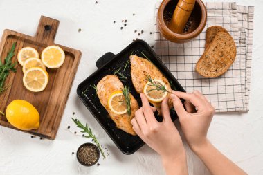 Female hands with fried chicken breast, spices and lemons on light background