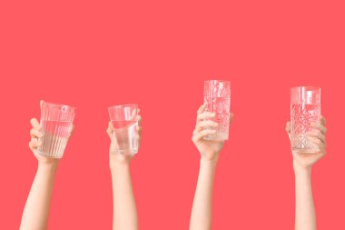 Female hands with different glasses of water on red background, closeup