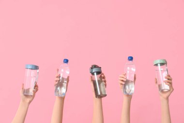 Female hands with different bottles of water on pink background
