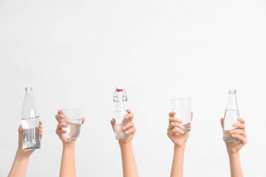 Female hands with bottles and glasses of water on white background, closeup