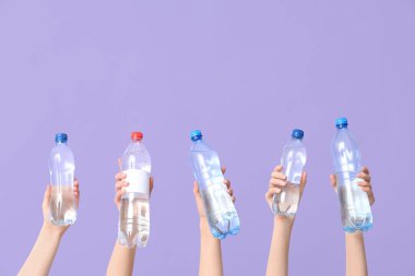 Female hands with different bottles of water on lilac background