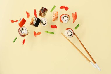 Bej arka planda lezzetli uçan suşi ruloları, zencefil ve çubuklar.
