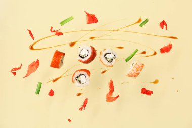 Bej arka planda lezzetli uçan suşi ruloları, sos ve zencefil.