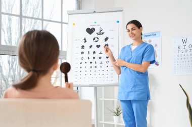 Female ophthalmologist checking little girl's eyesight near test chart in clinic clipart